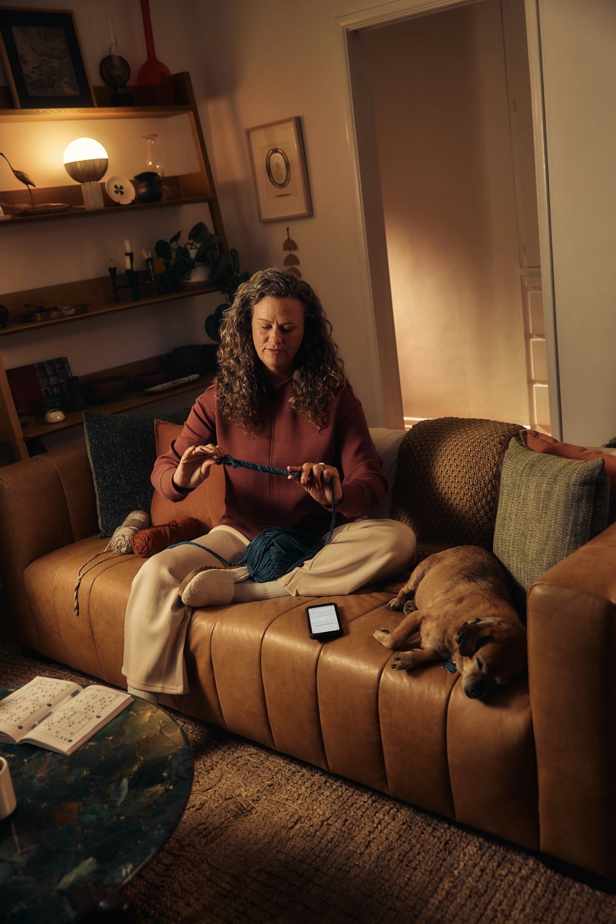 Woman knitting on couch with dog sleeping nearby